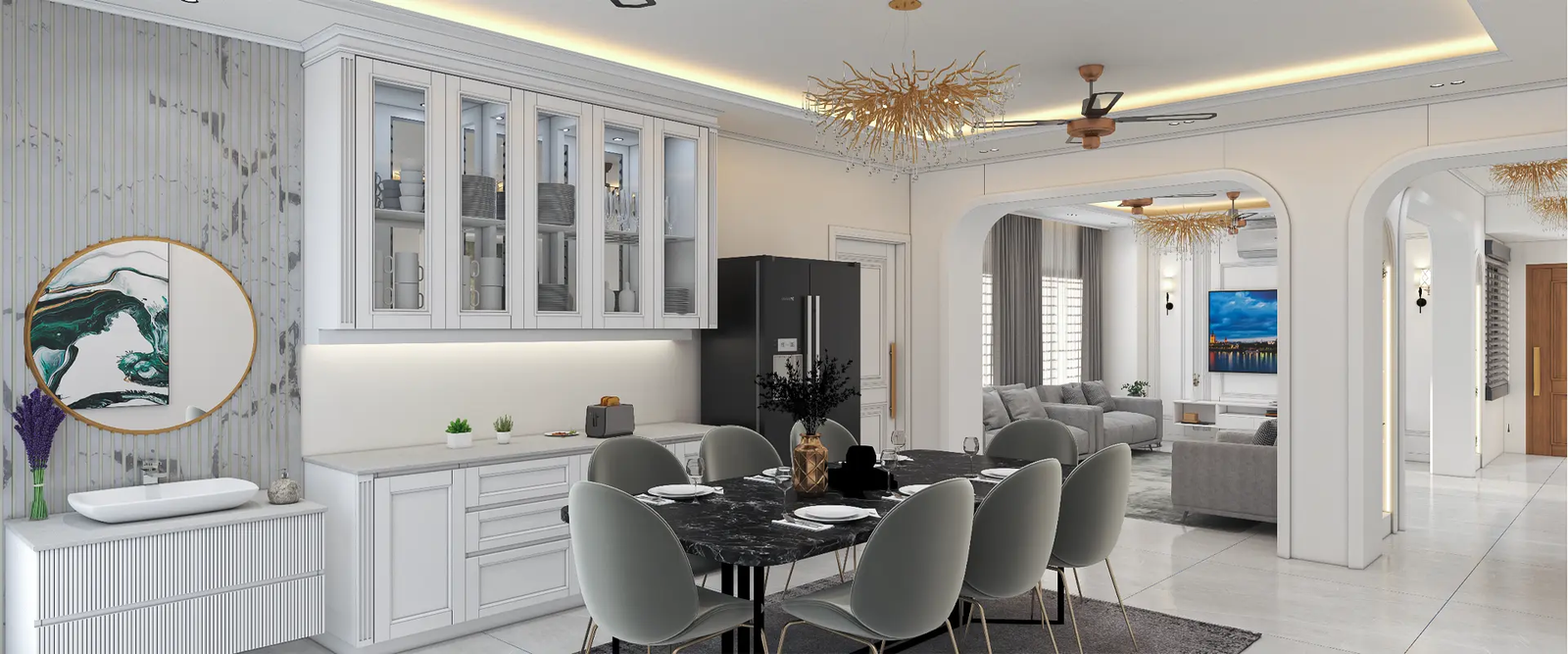 A modern, open-concept dining and living area showcasing sophisticated elegance. The dining space features a black marble dining table with six grey upholstered chairs, beautifully set with plates and glasses. A striking gold chandelier with a branch-like design hangs above the table, adding a luxurious touch. Adjacent to the dining area, the kitchen boasts white cabinetry with glass-fronted upper cabinets, a sleek black refrigerator, and a pristine white countertop. A decorative round mirror with a gold frame and an abstract art piece adorn the wall above a white console with a sink. The living area, visible through an arched doorway, includes a grey sofa set, a wall-mounted TV, and large windows draped with grey curtains that allow natural light to flood the space. The overall design is cohesive, with a neutral color palette, modern furnishings, and elegant lighting fixtures, creating a stylish and inviting home interior.