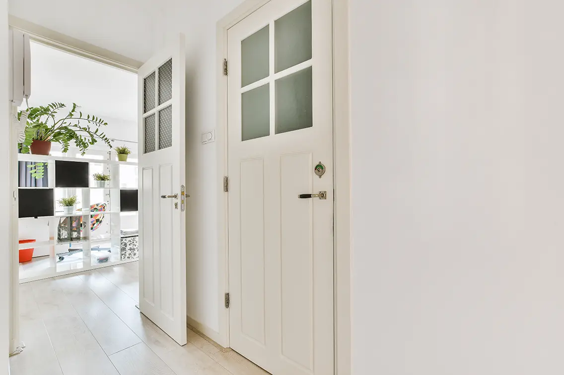 Two white modern doors. One of the doors lead to a room decorated with plants. It creates a serene ambiance.